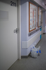 in a corridor of a hospital ward there are empty urine bottles in front of a patient's room