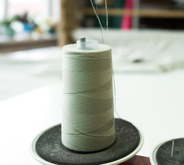 Close-up of a spool of thread on the industrial sewing machine. A seamstress workplace with a spool of threads. Selective focus.