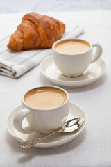 two coffees and a croissant on the table. breakfast on a sunny day
