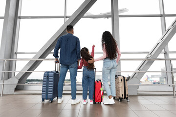 Family With Daughter Looking At Plane Departure Out Of Window In Airport