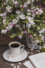 A beautiful postcard. A white coffee cup with a saucer, a statuette, candles, a book and a vase with a bouquet of blooming apple trees. Beautiful still life. Spring time. The concept of 