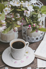 A beautiful postcard. A white coffee cup with a saucer, a statuette, candles, a book and a vase with a bouquet of blooming apple trees. Beautiful still life. Spring time. The concept of 