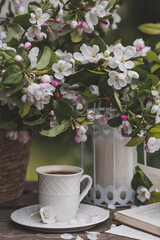 A beautiful postcard. A white coffee cup with a saucer, a statuette, candles, a book and a vase with a bouquet of blooming apple trees. Beautiful still life. Spring time. The concept of 