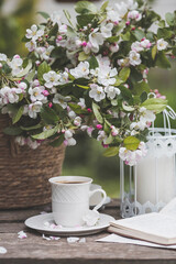 A beautiful postcard. A white coffee cup with a saucer, a statuette, candles, a book and a vase with a bouquet of blooming apple trees. Beautiful still life. Spring time. The concept of 