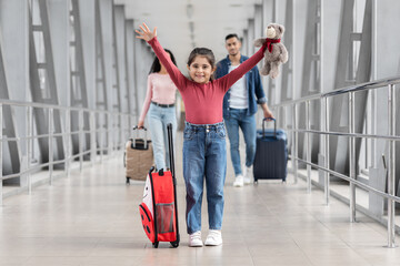Fototapeta na wymiar Happy Excited Little Girl Standing At Airport, Enjoying Vacation Travel With Parents