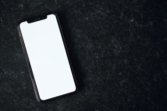 Mockup image of a mobile phone with a blank white screen. Mobile phone on a black background. Phone on stone.