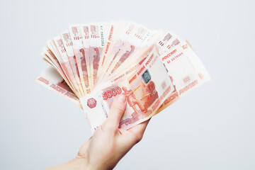 A woman's hand holds banknotes of five thousand rubles folded in a fan on a white background