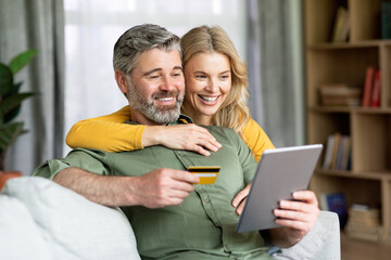 Happy Middle Aged Couple Using Digital Tablet And Credit Card At Home