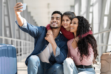 Joyful Middle Eastern Family Of Three Taking Selfie With Smartphone In Airport