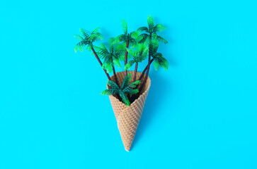 Palm trees going out of an ice cream cone against blue background. Minimal surreal concept for...