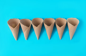 Ice cream cones neatly aligned against blue background. Minimal concept for summer sweets or ice cream shop. Design for banner or editorial.