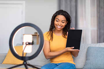 Joyful black female blogger filming video review of modern digital tablet, talking to cellphone webcamera - obrazy, fototapety, plakaty