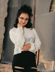 Dark haired woman poses in white knit top in front of broken mirror