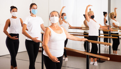 Fototapeta premium Women of different ages in face masks exercising ballet moves in training room.