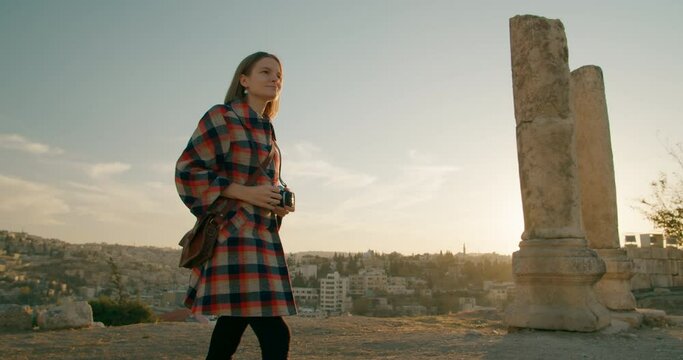 Photographer Woman takes Pictures Amman Citadel - landmark in capital of Jordan. Female Tourist travels with Retro Film Camera. Middle East Cityscape at sunset. 4K wide tracking shot