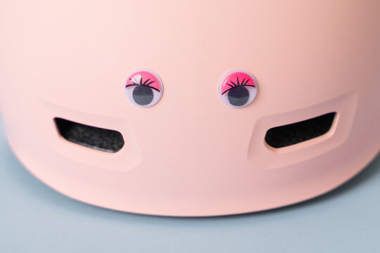 Pink helmet with funny doll eyes on blue background. Childs outdoors activity safety protection 