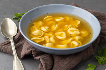 Cappelletti or tortellini brodo soup in a bowl with seasoning over stone background