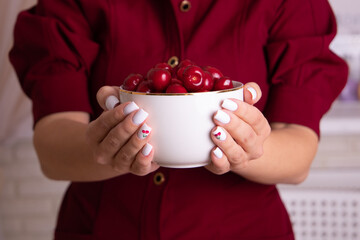 Female hands with white manicure nails holding bowl with sweet cherries