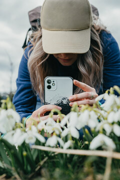 Young girl with hat taking take pictures of flowers with phone