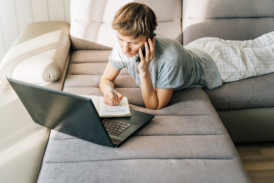 Woman lies on couch, talking on the phone and taking notes