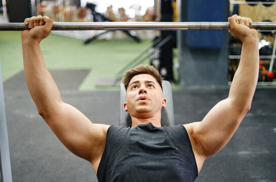 Young Man Exercising In Gym With Bench Press