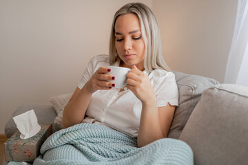 Sick woman sitting under the blanket. Sick woman with seasonal infections, flu, allergy lying in bed. Sick woman covered with a blanket lying in bed with high fever and a flu, resting and drinking tea