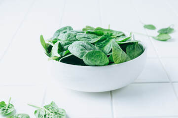 Fresh baby spinach in a white bowl on rustic wooden background. Selective focus