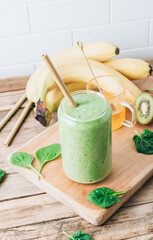 Green healthy smoothie in glass with banana, kiwi and spinach on rustic wooden background