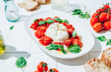 Salad with baked tomatoes and burrata on white tile background. Italian cuisine. Healthy eating. Vegetarian food
