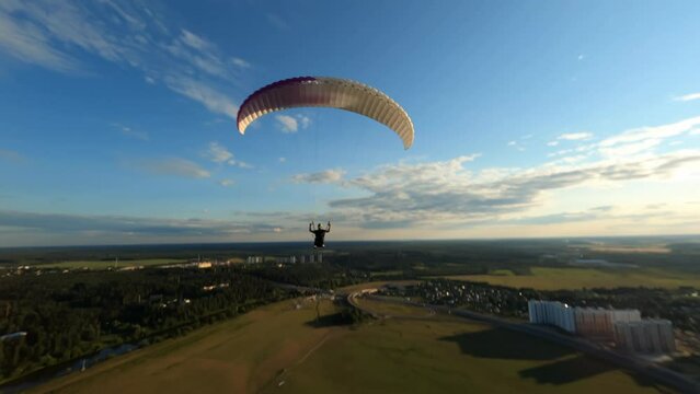Dynamic aerial shot of paraglider flying along the river and against sunset sky 