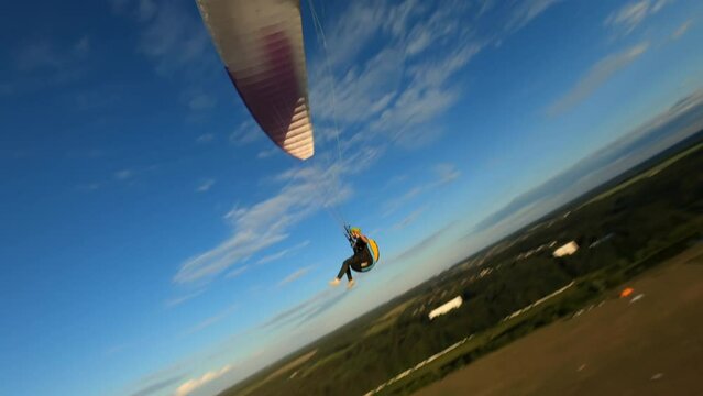 Dynamic aerial shot of paraglider flying along the river and against sunset sky 