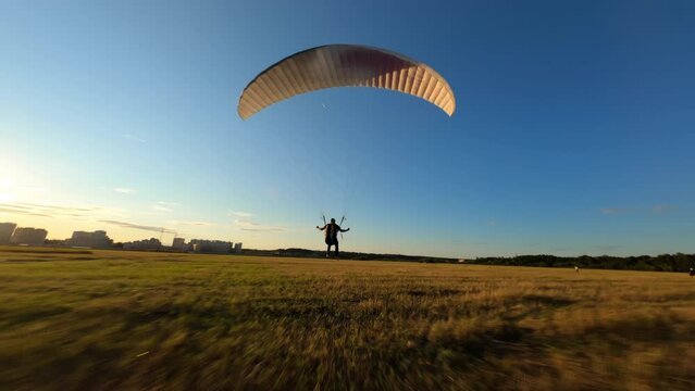 Paraglider lands on the green field while colourful sunset or sunrise sky 