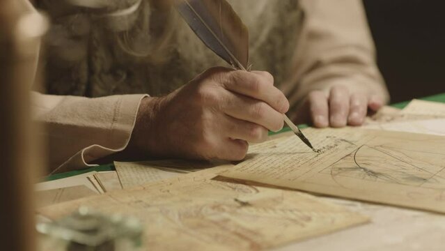 Old man with beard dressed like Leonardo Da Vinci writing , painting and working in vintage 15 - 16 century designed room . Big drawing of famous artwork  . Dipping ink pen on inkwell . Slow motion 
