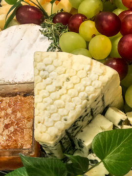 Queijo brie, queijo gorgonzola, queijo parmes&atilde;o, favo de mel, uvas verdes e roxas com or&eacute;gano fresco decorando.