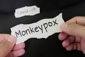 Monkeypox virus disease next covid concept. Hand holding paper with word monkeypox in black background with covid-19 word behind.