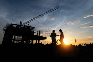 Fototapeta na wymiar Engineers and workers inspecting projects at the construction site background. Construction site at sunset in the evening, Asian engineer silhouette