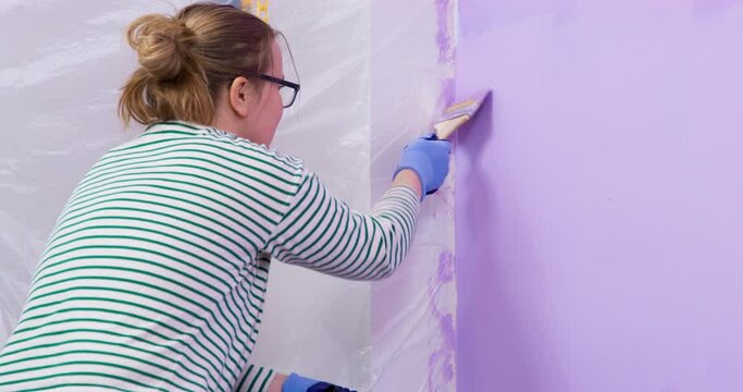 Painter woman paints wall with roller and brush in very peri color. Professional repair and painting of walls. Designer color renovation of interior. Close-up painting the walls with roller and brus.