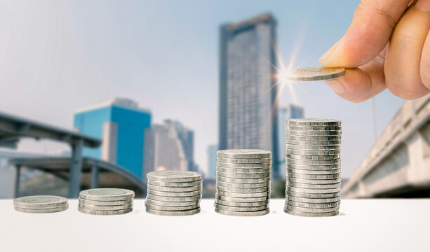 Man hand stacked coins with money saving concept and profit graph business finance in a piggy bank with money boxes for future funds of tourism, home, and retirement on a blurred background.