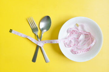 Fork and spoon wrapped with measuring tape flat lay in yellow background. Anorexia, Diet and nutrition to lose weight concept.