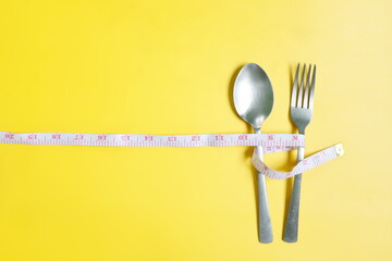 Fork and spoon wrapped with measuring tape flat lay in yellow background. Anorexia, Diet and...
