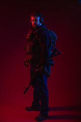 Naklejka premium airsoft player in full gear with guns GG RK74. a man in headphones, body armor, with a backpack and a belt. red background. colored, blue-red light