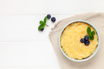 Corn porridge with berries in a bowl on the table. Baby food. Healthy breakfast. Top view. Copy space