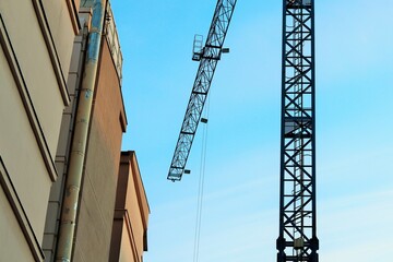 Fototapeta na wymiar Construction crane against the background of the blue sky and the wall of the building under construction