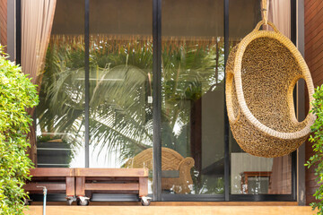 A wicker armchair in the form of a cocoon suspended on the terrace. The recreation scene, the concept of travel and recreation.