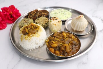 Indian vegetarian lunch or dinner Thali includes beans sabzi, dal rice, Alu Vadi, dhokla, veg cutlet, raita, and ukdiche modak.  Indian food is served on a plate or thali. Ganesh Jayanti Food. Copy