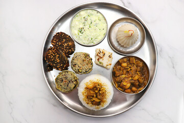 Indian vegetarian lunch or dinner Thali includes beans sabzi, dal rice, Alu Vadi, dhokla, veg cutlet, raita, and ukdiche modak.  Indian food is served on a plate or thali. Ganesh Jayanti Food. Copy