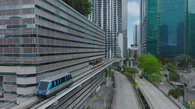 Futuristic city borough with modern high rise buildings and automatic passenger transport rail vehicle. Metromover stopping at station. Miami, USA