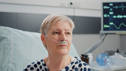 Close up of aged woman sitting in bed with heart rate monitor at clinic. Portrait of patient with...