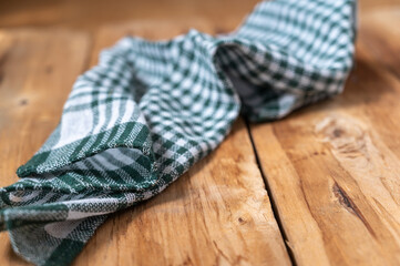 Fototapeta na wymiar A green checkered kitchen towel lies on the countertop of a wooden table. Crumpled Towel or kitchen napkin on rough boards. Selective Focus.
