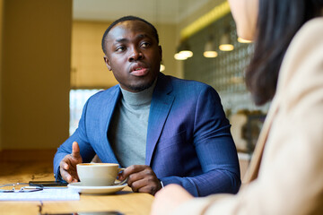 Fototapeta na wymiar African young businessman in suit talking to his colleague during coffee break at cafe